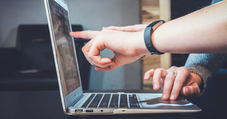 Das Bild zeigt eine Szene zum Thema Werkzeuge für digitales Onboarding: einen aufgeklappten Laptop, davor zwei Arme von zwei Personen. Die eine Person zeigt der anderen etwas am Bildschirm.